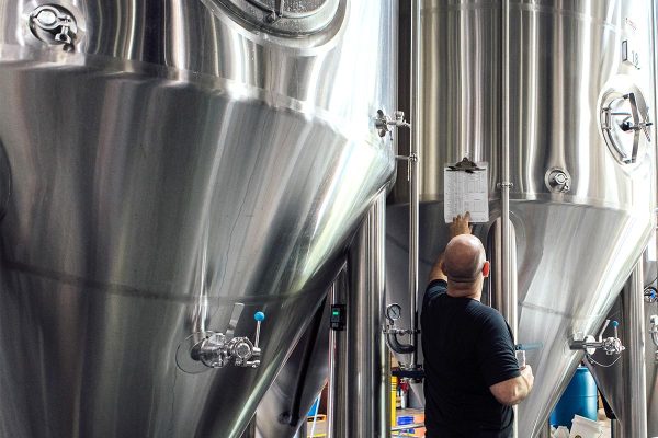 Brewer in front of fermenter tanks looking at beer recipe