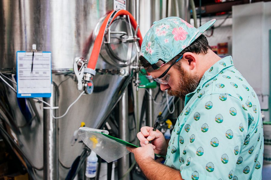 man writing on clipboard in brewery
